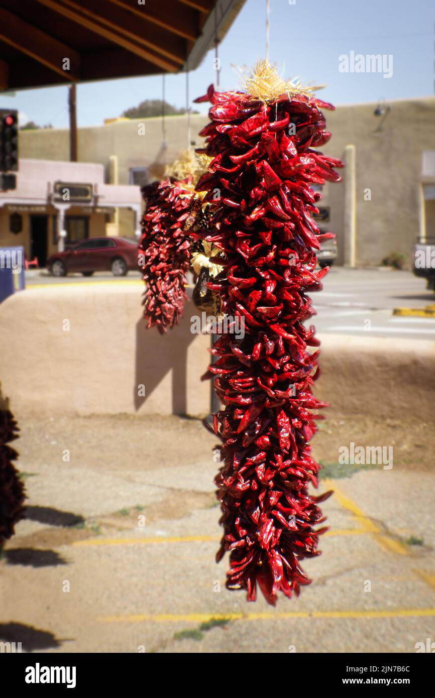Cuerdas de pepers rojos secos colgando al aire libre en el suroeste de EE.UU. adobe ciudad - enfoque selectivo Foto de stock