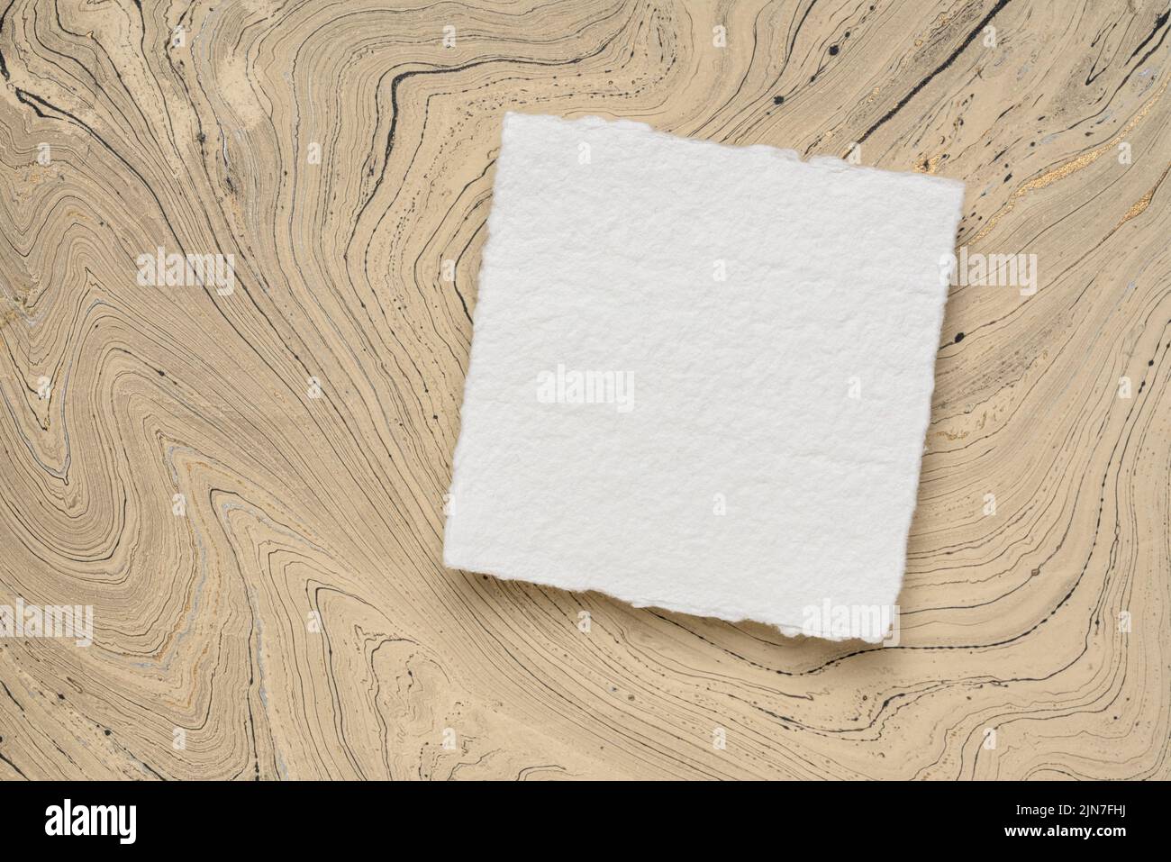 Pequeña hoja cuadrada de papel blanco Khadi contra papel de mármol Foto de stock