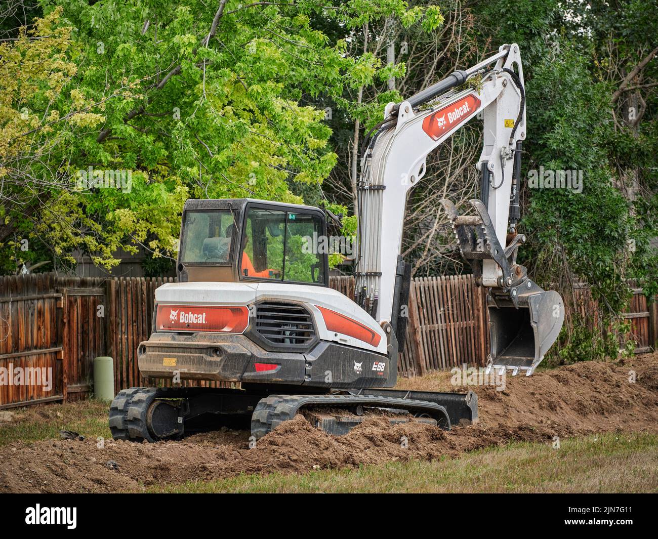 Fort Collins, CO, EE.UU. - 21 de julio de 2022: E88, la excavadora compacta Bobcat más grande que trabaja en un área residencial a lo largo de una valla de patio trasero. Foto de stock