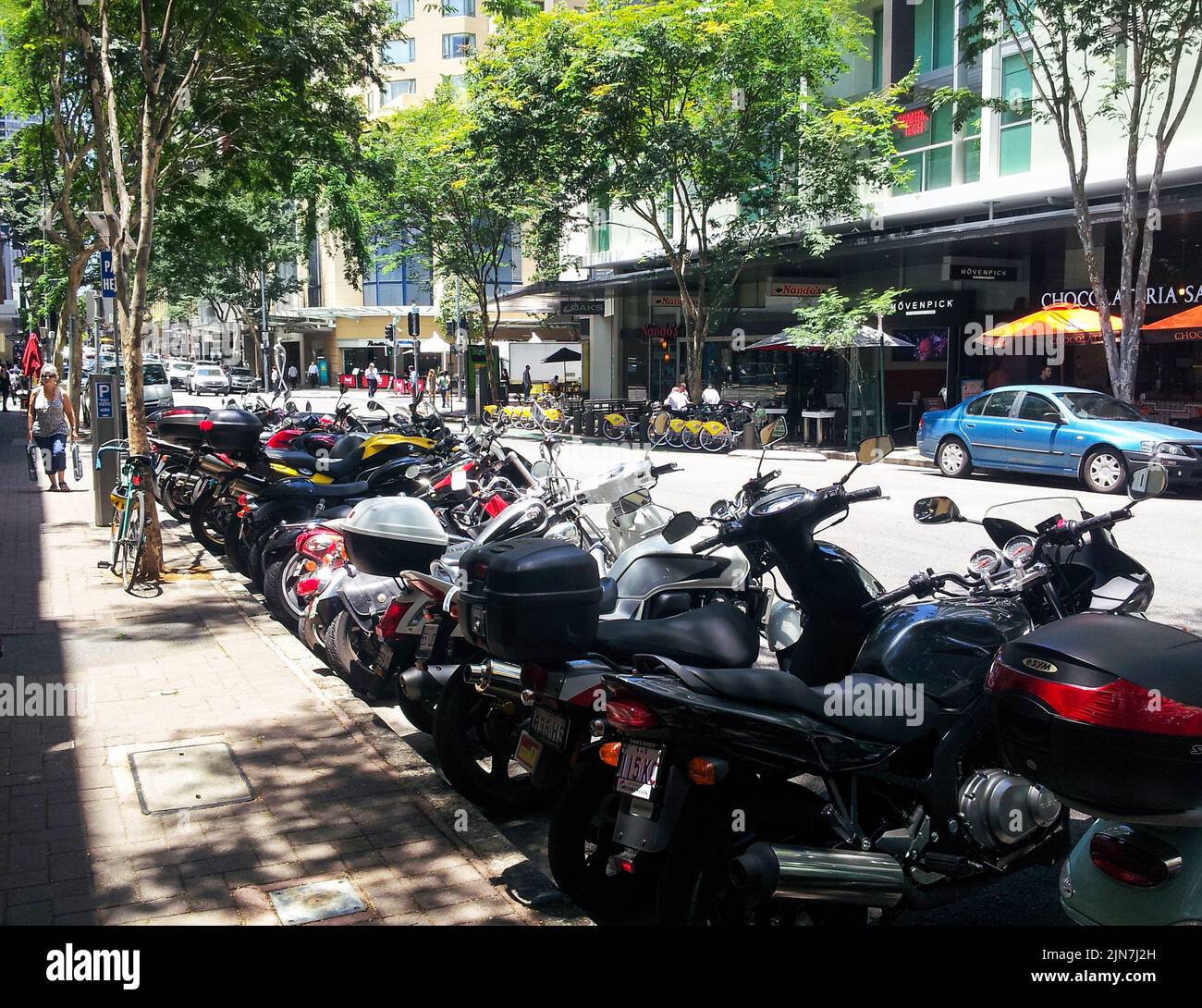 Calle urbana con motocicletas estacionadas a lo largo de un lado y para alquilar bicicletas y coches en el otro en Brisbane Queensland Australia Nov 21 2013 Foto de stock
