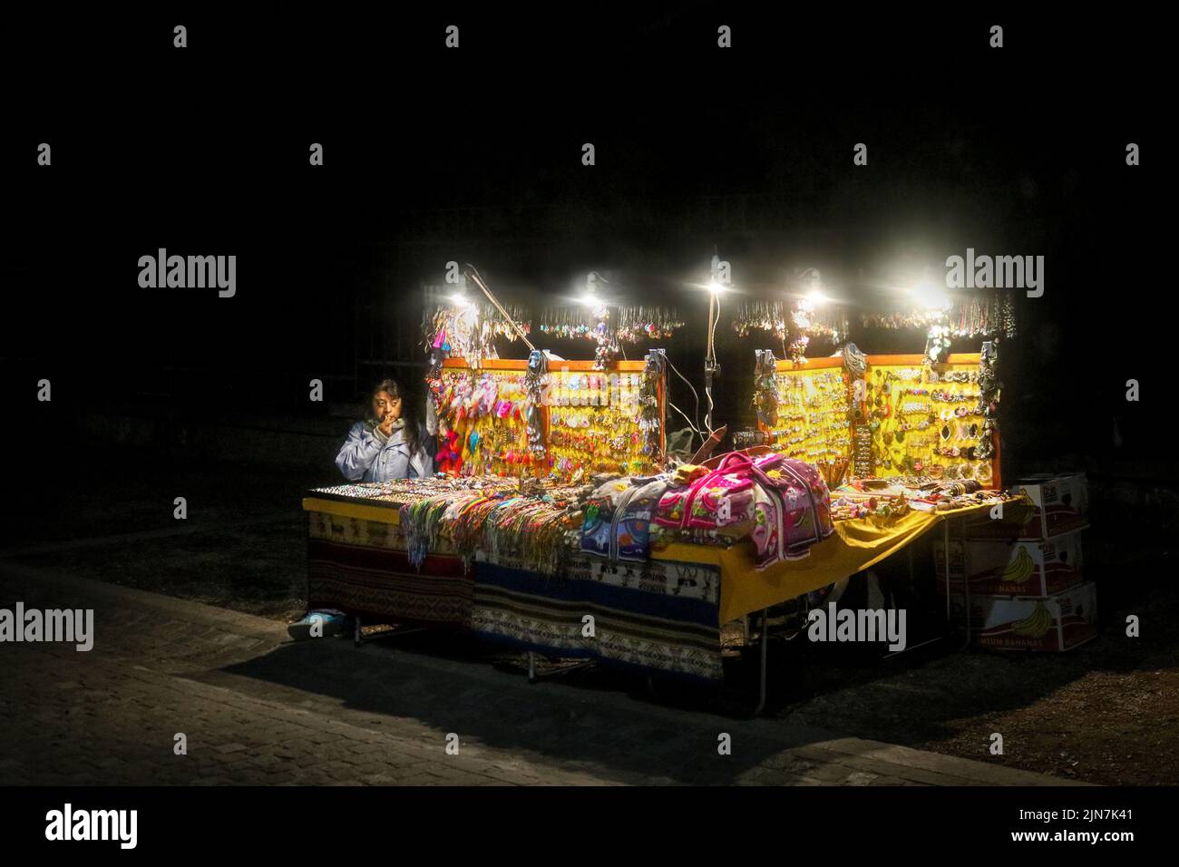 Vendedor sentado en una mesa al aire libre iluminada mostrando joyas y otros recuerdos por la noche en Atenas, Grecia Foto de stock