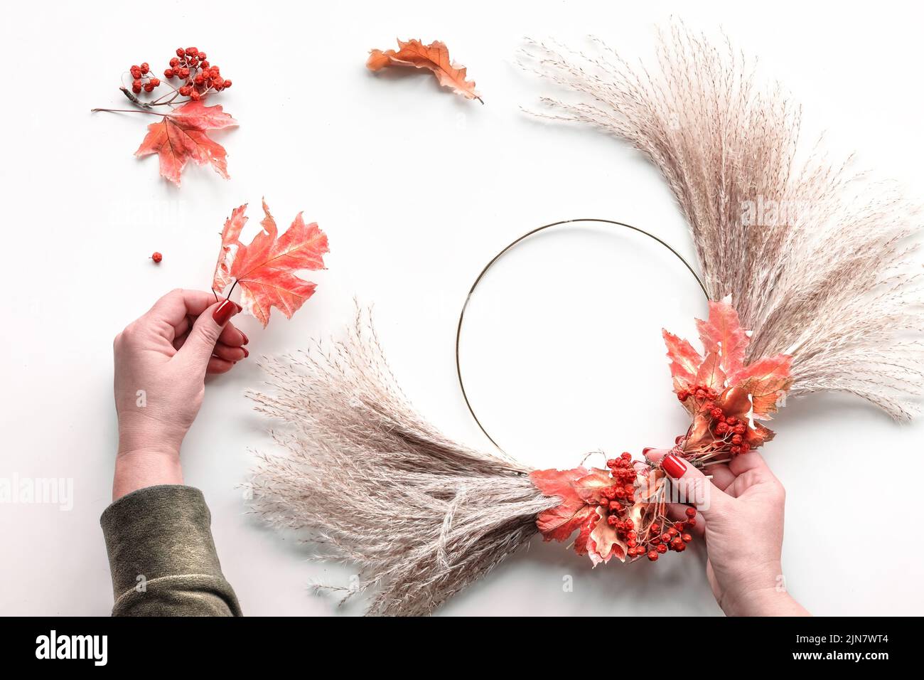 Corona floral de pasto pampas seco y hojas otoñales. Las manos atan las decoraciones al marco de metal. Foto de stock