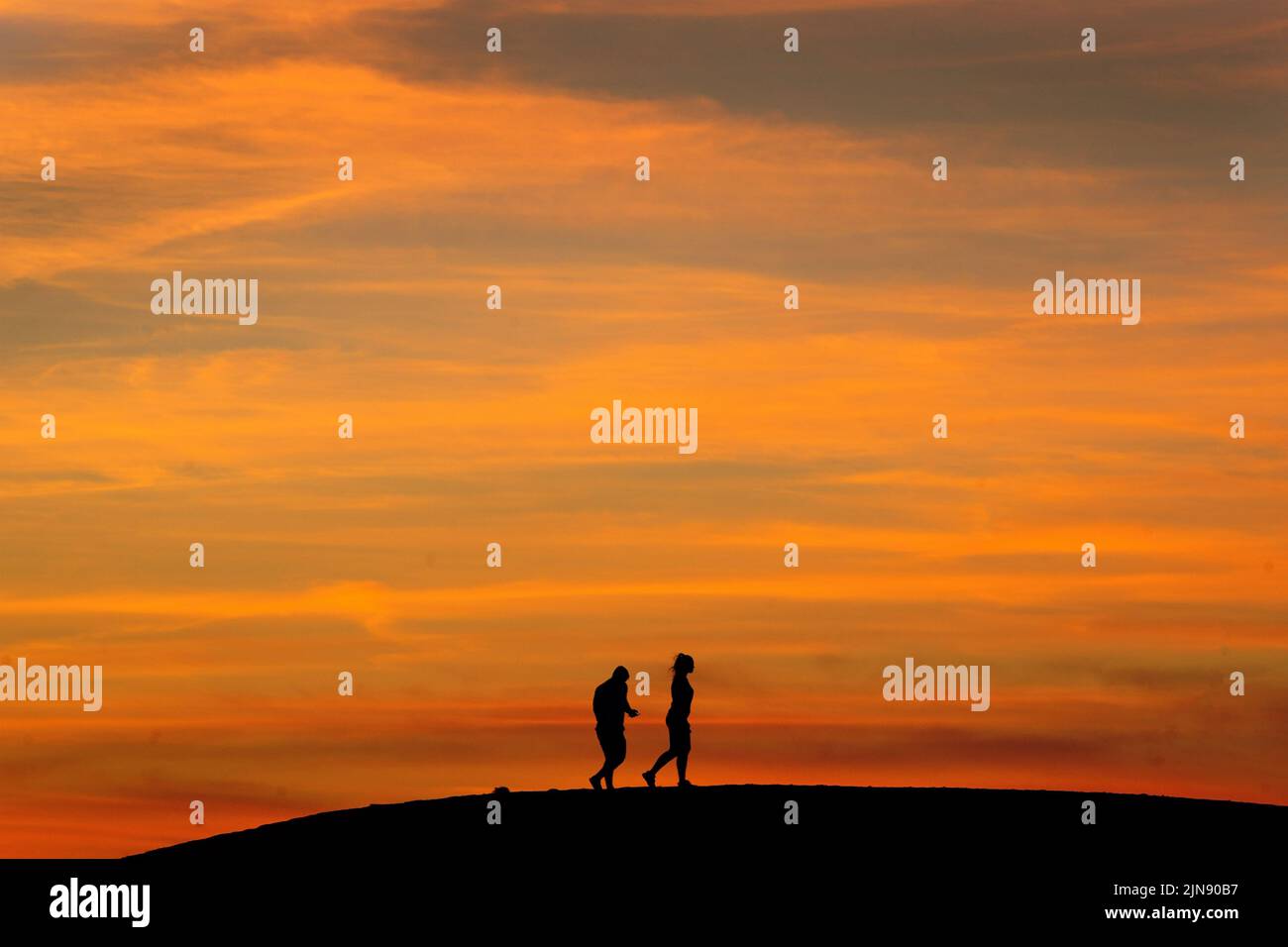 Un par de personas caminan por una colina después de la puesta de sol en Ealing, al oeste de Londres, mientras continúa un verano de prohibiciones de tubos de escape y advertencias de incendio, con una alerta de salud por calor que entra en vigor en gran parte del país. Fecha de la foto: Martes 9 de agosto de 2022. Foto de stock