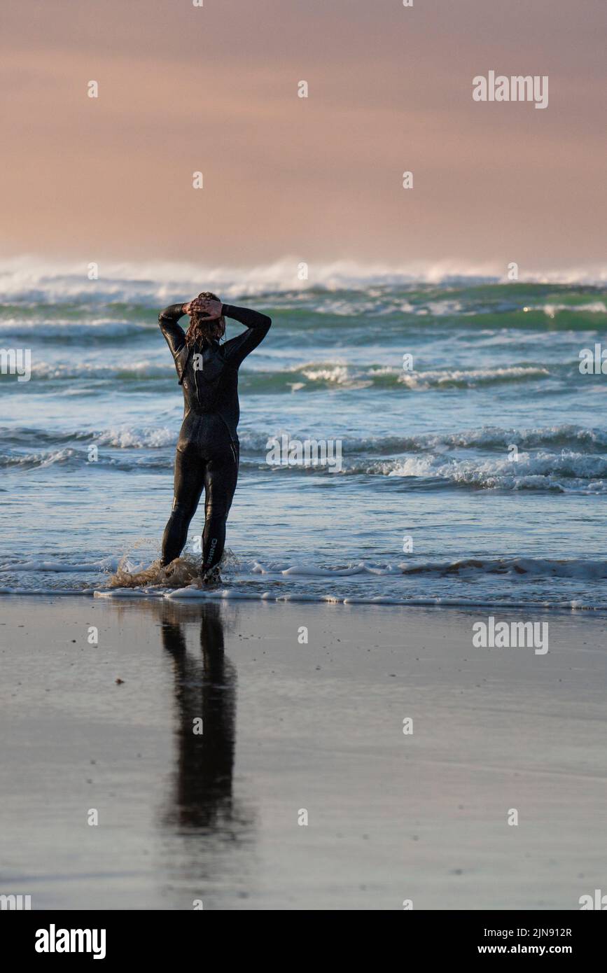 Un hombre que llevaba traje de neopreno parado solo en la costa de Crantock Beach en Newquay en Cornwall. Foto de stock