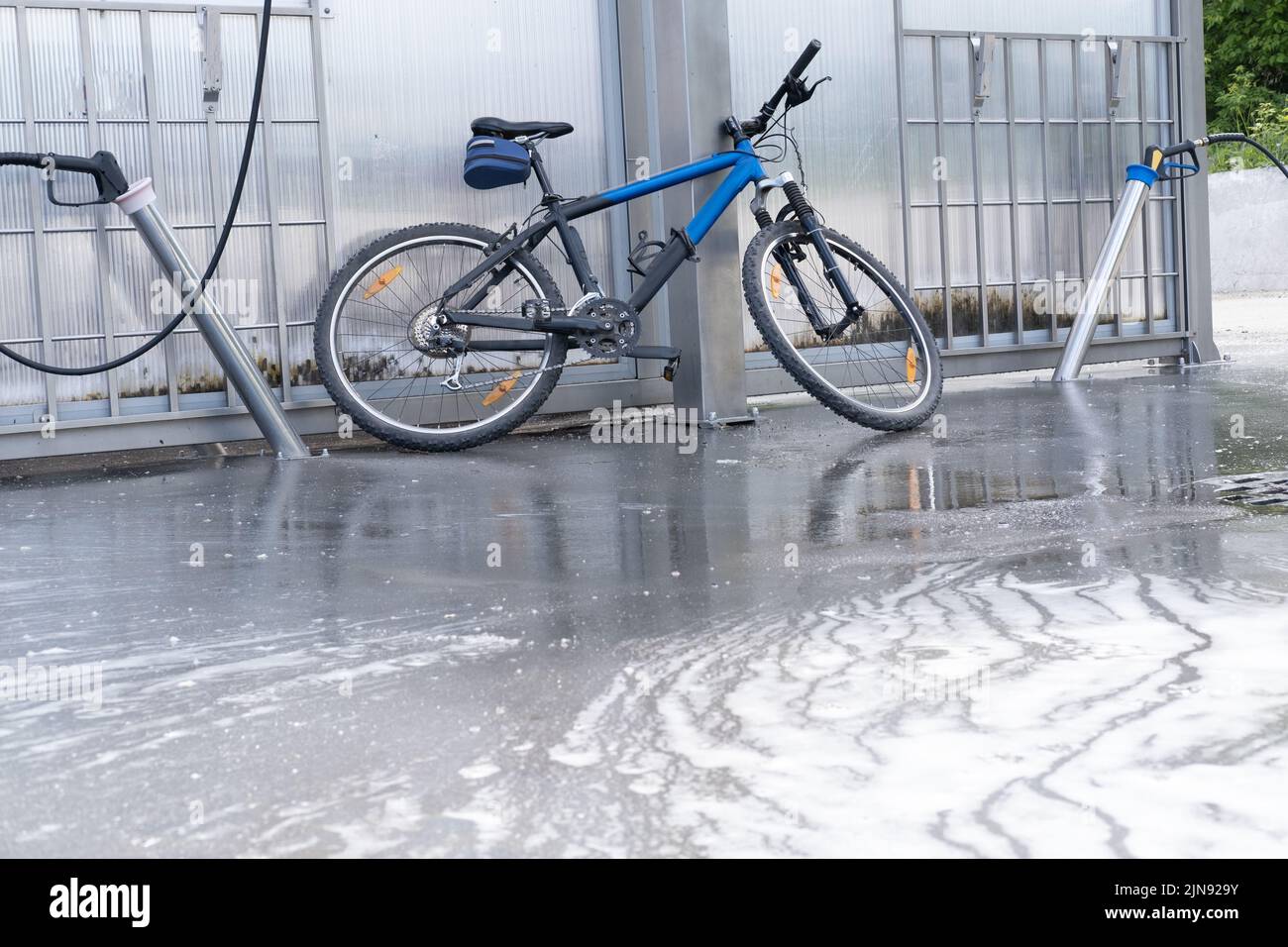 Lavar una bicicleta con un chorro de espuma en un lavado de coches. La bicicleta está cubierta de espuma. Autoservicio. Mantenimiento de bicicletas. Foto de stock
