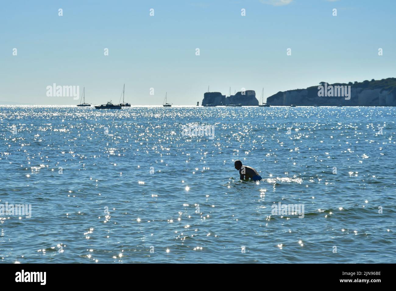 Studland Beach, Shell Bay, Dorset, Reino Unido, 10th de agosto de 2022, El tiempo. Caluroso y soleado al comienzo de otra ola de calor. Un hombre se da un baño en el mar bajo la luz del sol de la mañana. Crédito: Paul Biggins/Alamy Live News Foto de stock