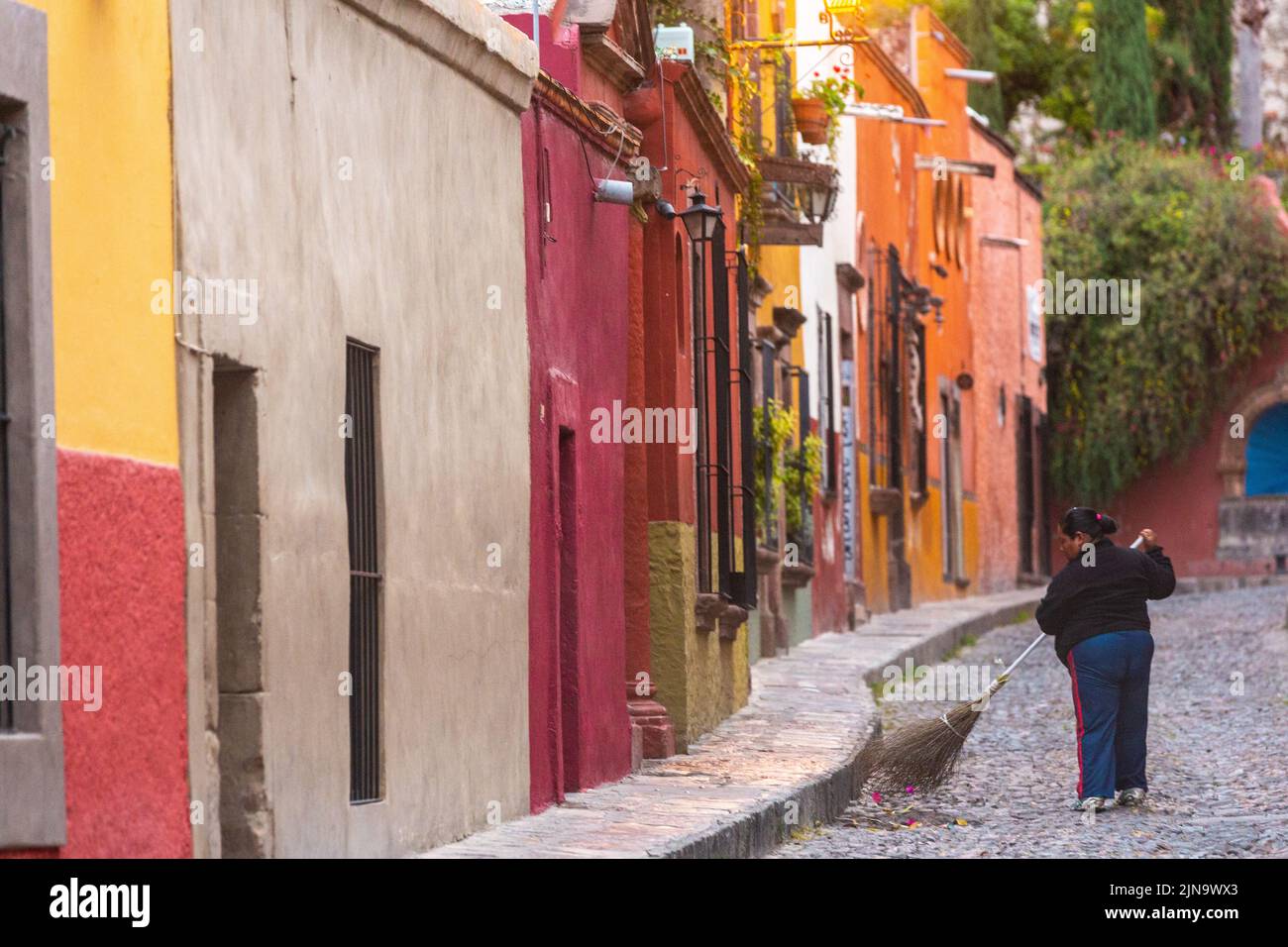 Un limpiador de calles barre las calles adoquinadas de la Calle Aldama temprano en la mañana en el centro histórico de la ciudad de San Miguel de Allende, México. Foto de stock