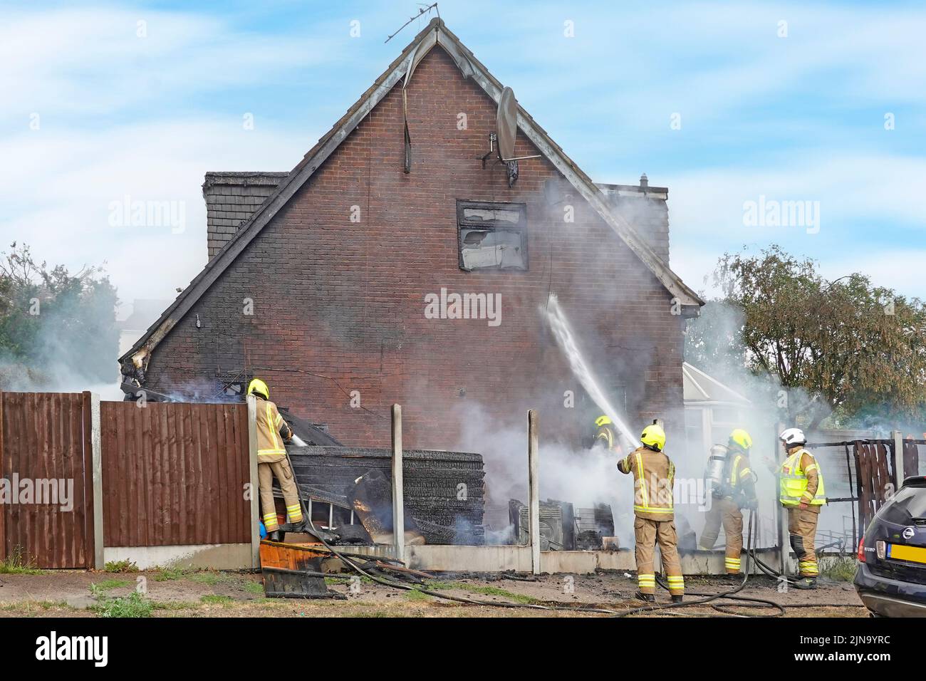 Servicio de Bomberos y Rescate de Essex Bomberos en ropa de protección peligrosa y peligrosa casa de trabajo contra incendios amortiguando la pared y los escombros Inglaterra Reino Unido Foto de stock