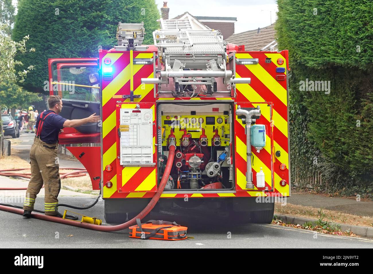 Servicio de bomberos y rescate de Essex atendiendo a la brigada de bomberos casa cerca vista trasera válvulas de motor contra incendios con conexión de manguera y bombero Inglaterra Reino Unido Foto de stock