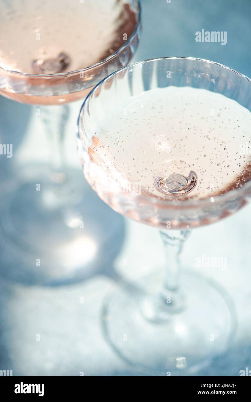 Vino espumoso rosado o champán en copas de cristal sobre fondo blanco de hormigón en días soleados Foto de stock