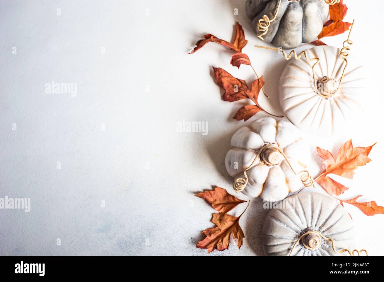 Concepto de tarjeta otoñal con calabaza de cerámica y hojas secas sobre fondo de hormigón Foto de stock