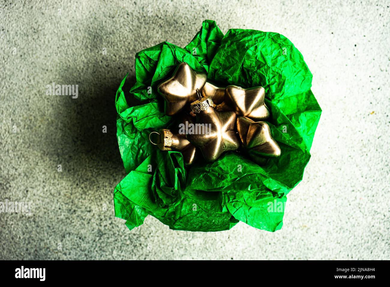 Caja de regalo rústica con bolas de Navidad en forma de estrella de bronce en papel de envoltura verde en la caja sobre fondo de hormigón Foto de stock