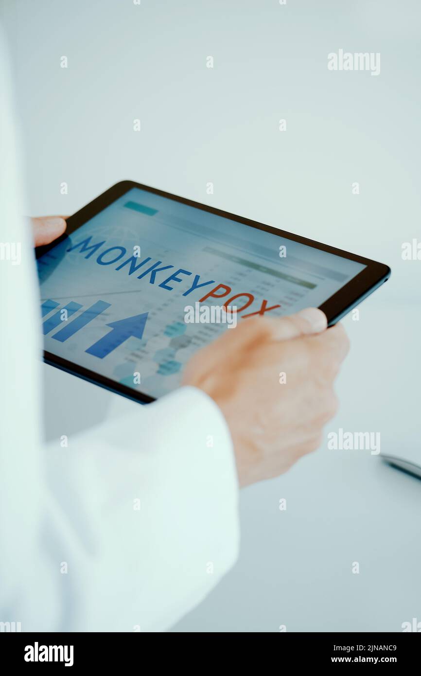 primer plano de un médico, con un abrigo blanco, en su oficina, teniendo una tableta digital en sus manos con el texto de la viruela del simio en su pantalla Foto de stock