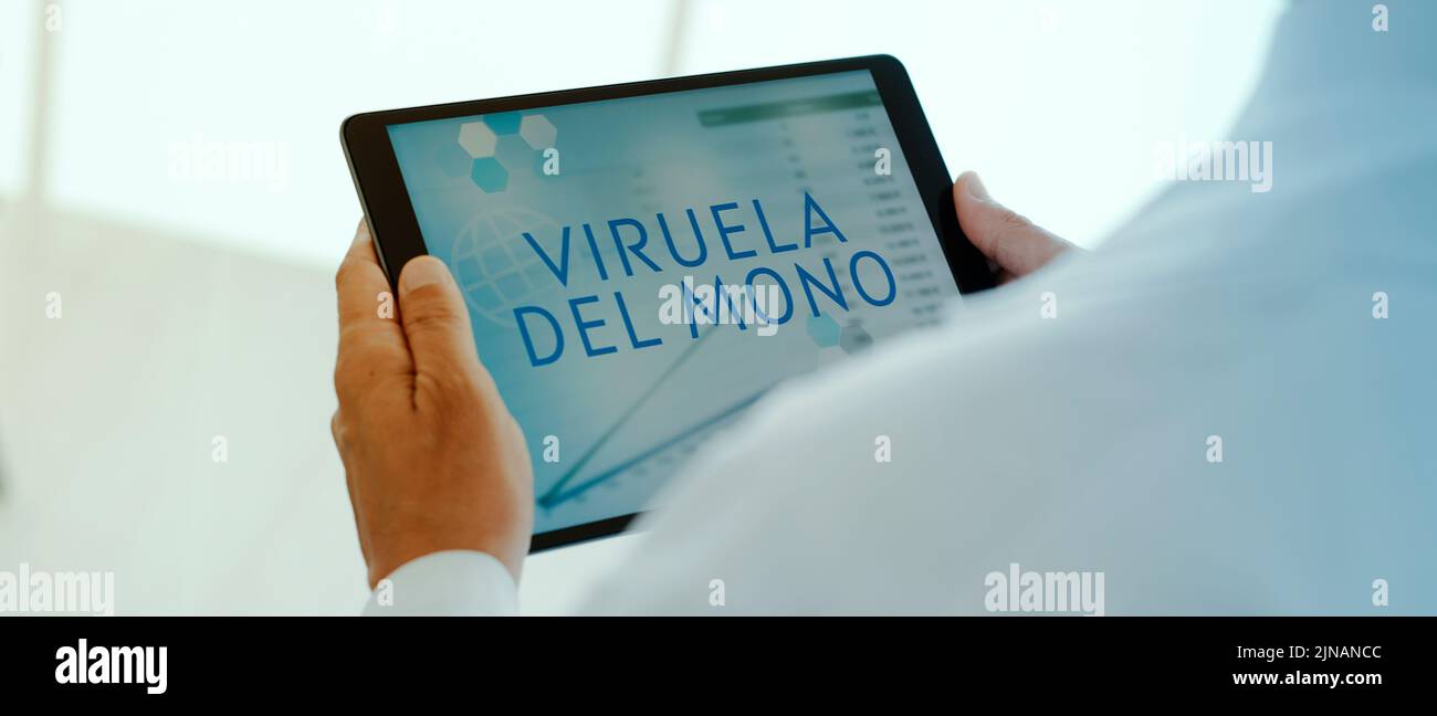 un doctor, con un abrigo blanco, tiene una tableta digital en sus manos con el texto monopox escrito en español en su pantalla, en formato panorámico Foto de stock