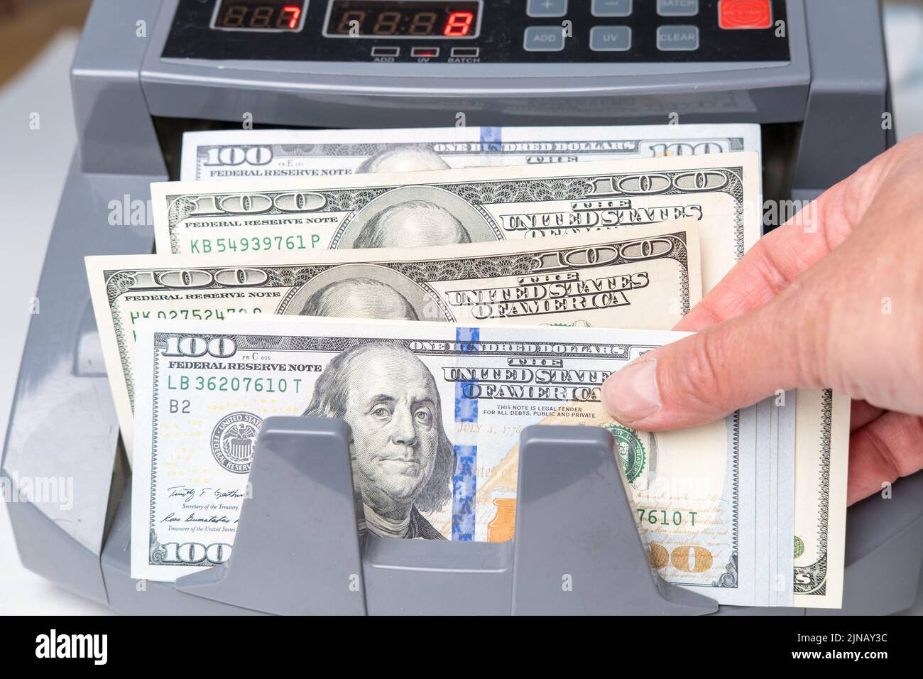La mano del empleado tomando dólares de la máquina de facturas. Contar dólares usando un contador de dinero electrónico en una sucursal bancaria o intercambiador de divisas. El Foto de stock