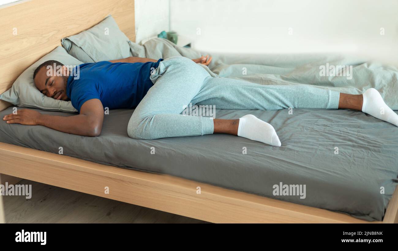 Black Guy durmiendo tumbado sobre el estómago en la cama en el dormitorio Foto de stock