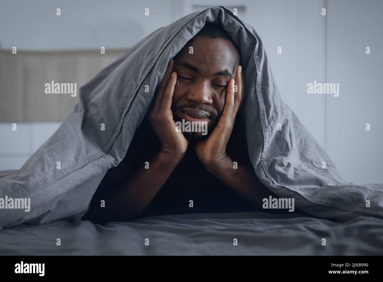 Hombre afroamericano soñoliento cubierto con manta en el dormitorio Foto de stock