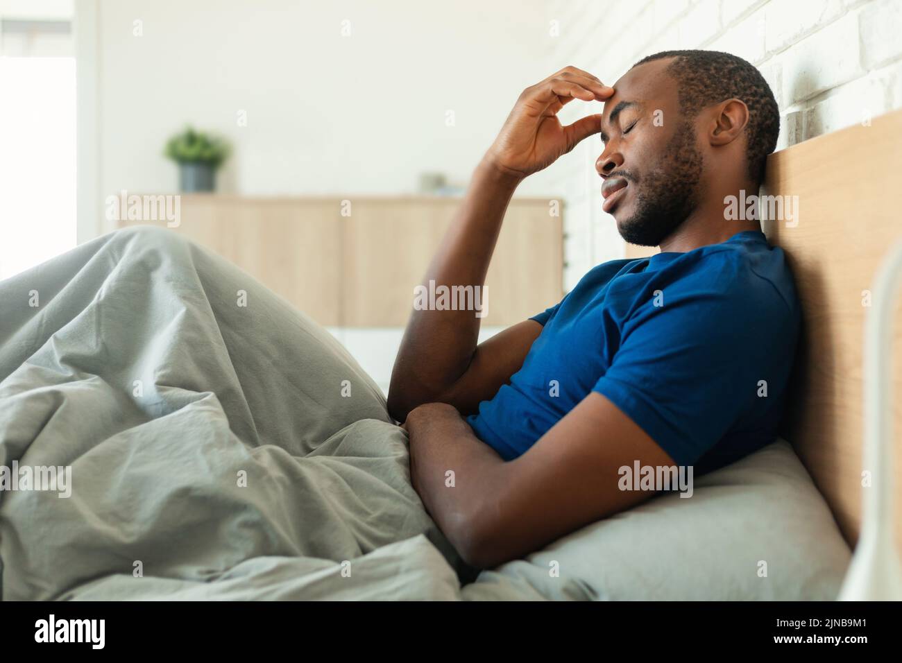 Hombre afroamericano con dolor de cabeza sentado en la cama en el dormitorio Foto de stock