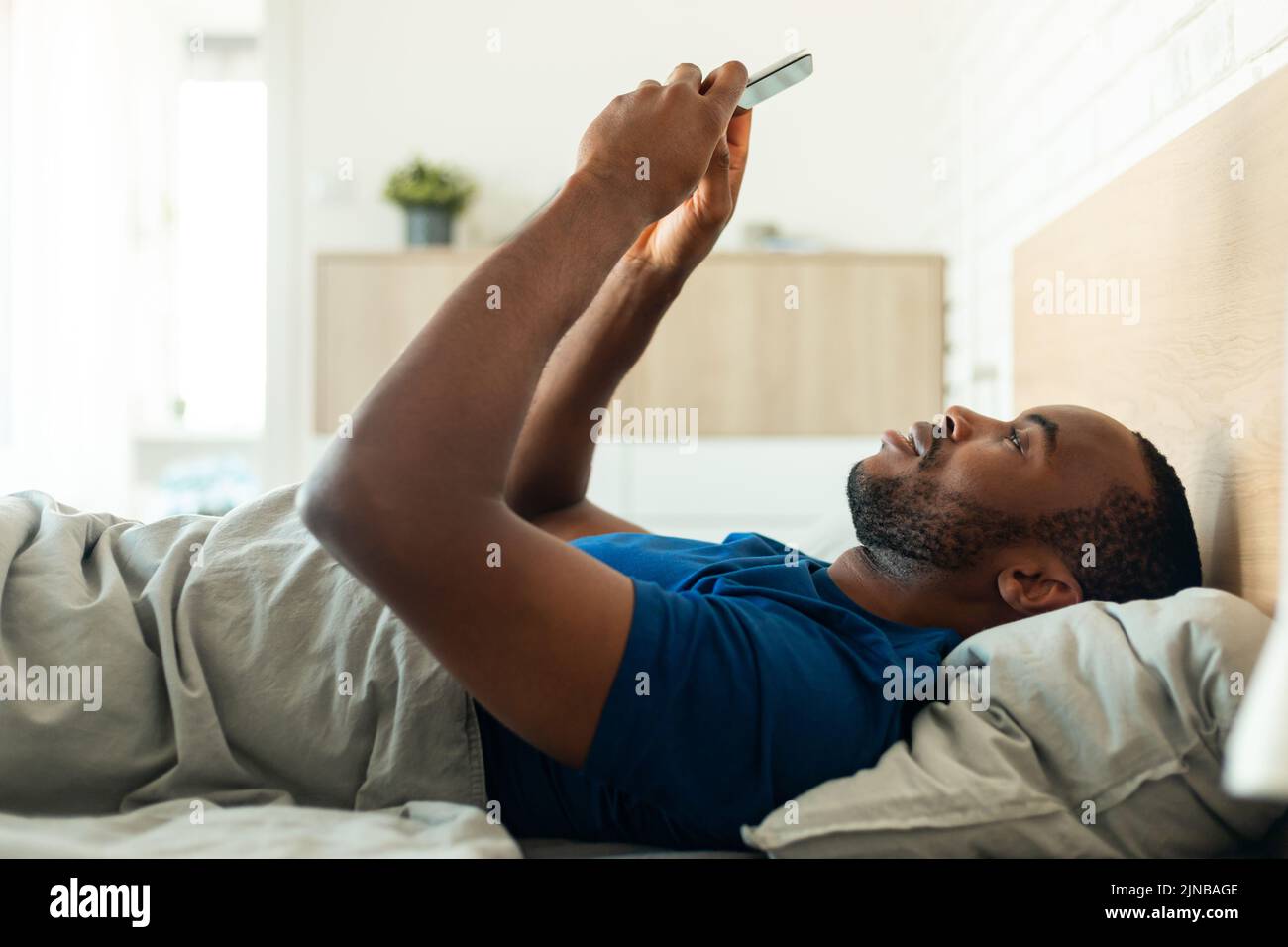 Hombre afroamericano utilizando el teléfono acostado en la parte de atrás en la habitación Foto de stock