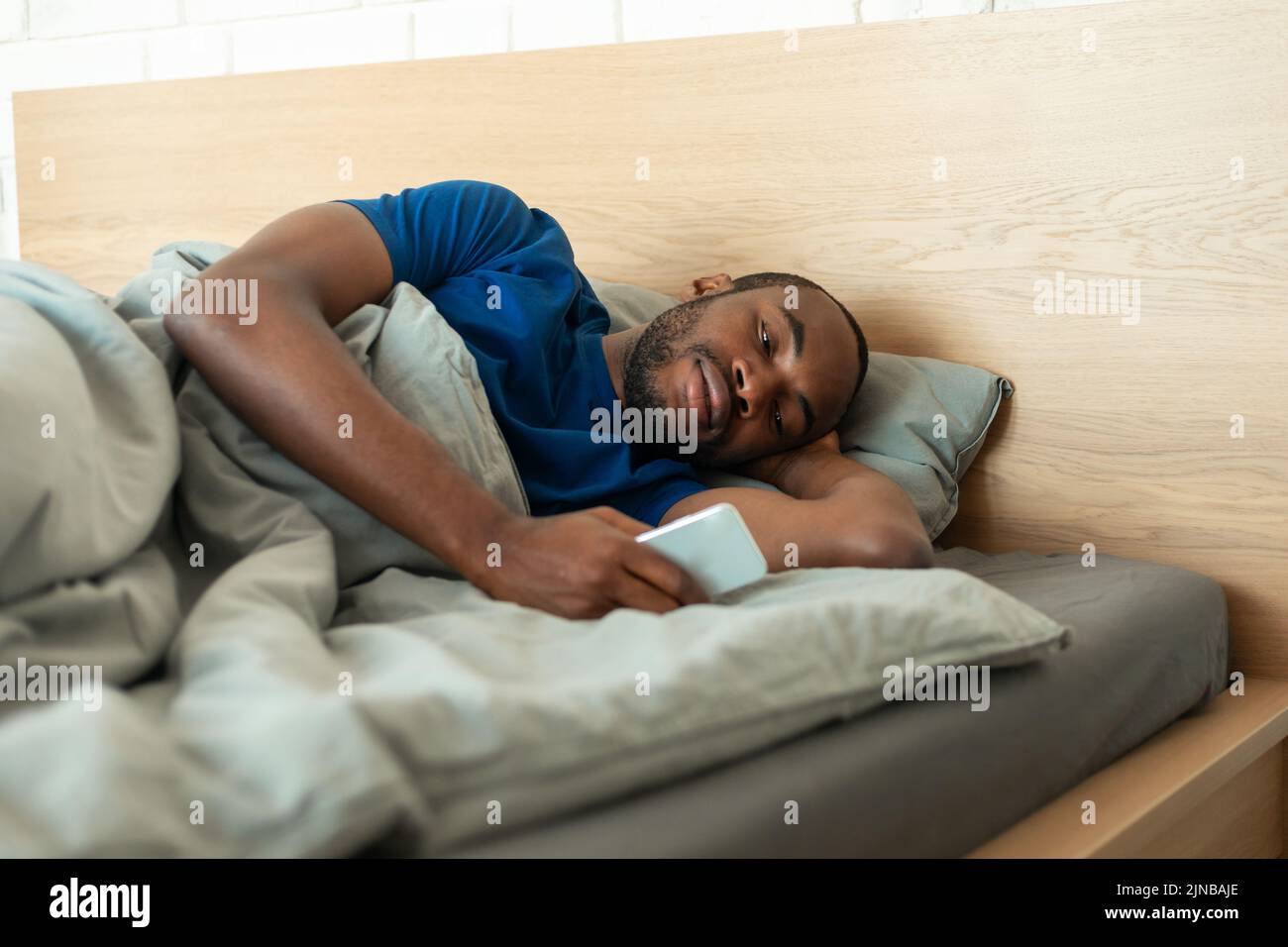 Hombre afroamericano que utiliza mensajes de texto por teléfono acostado en el dormitorio interior Foto de stock