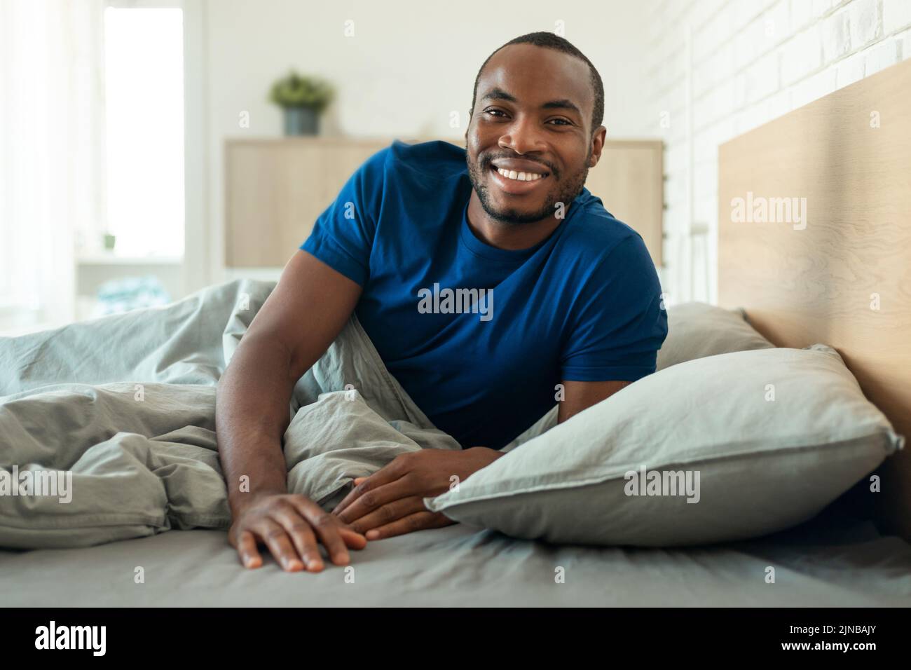 Feliz hombre afroamericano sonriendo tumbado en la cama en casa Foto de stock
