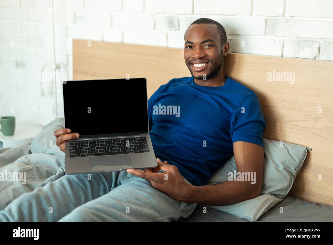 Hombre negro mostrando un ordenador portátil con pantalla en blanco en casa Foto de stock
