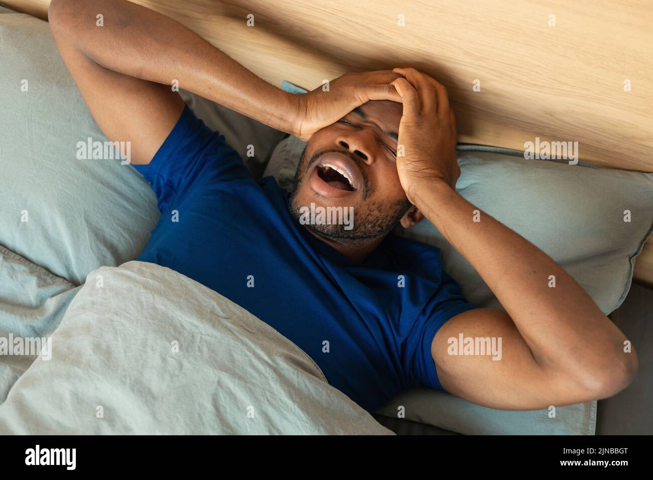 El hombre negro despierta bostezando y frotando los ojos acostado en el dormitorio Foto de stock