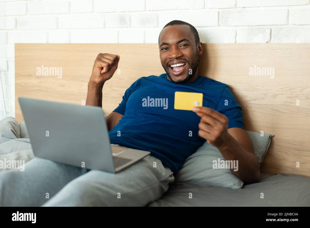 Alegre hombre negro usando el ordenador portátil que compra en línea Gesturing Sí interior Foto de stock