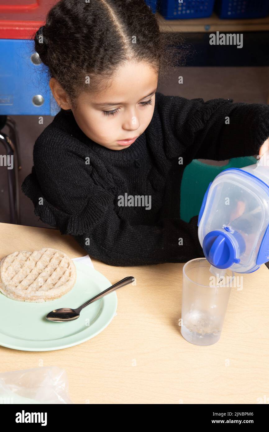 Educación Preescolar Cuidado Infantil Tiempo de comida niña de 4 años vertiendo agua propia en la mesa Foto de stock