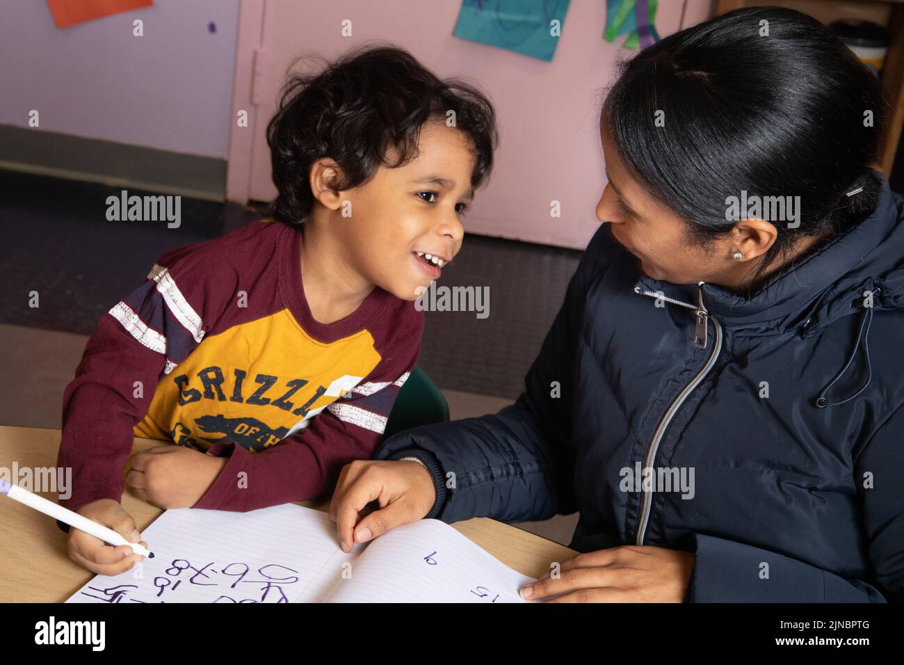 Educación Cuidado Infantil Preescolar Niño de 4 años con madre al comienzo del día escribiendo números en su libro de registro Foto de stock