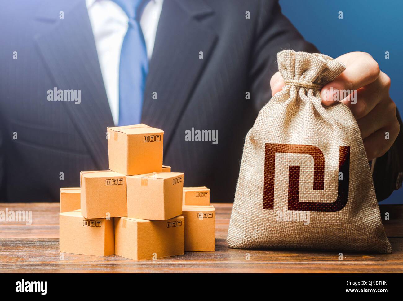 Un hombre de negocios sostiene una bolsa de dinero y cajas de shekel israelí con bienes. Importación y exportación. Ingresos de la empresa. Pago de impuestos y tasas. Presupuesto de publicidad. PU Foto de stock