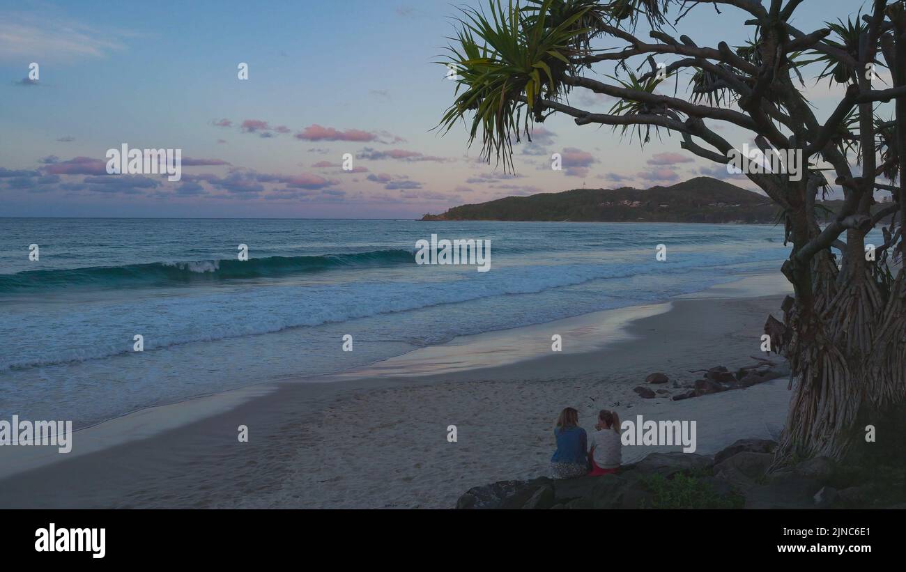 una puesta de sol en la playa principal con el faro de cape byron en la distancia en byron bay en el norte de nueva gales del sur, australia Foto de stock