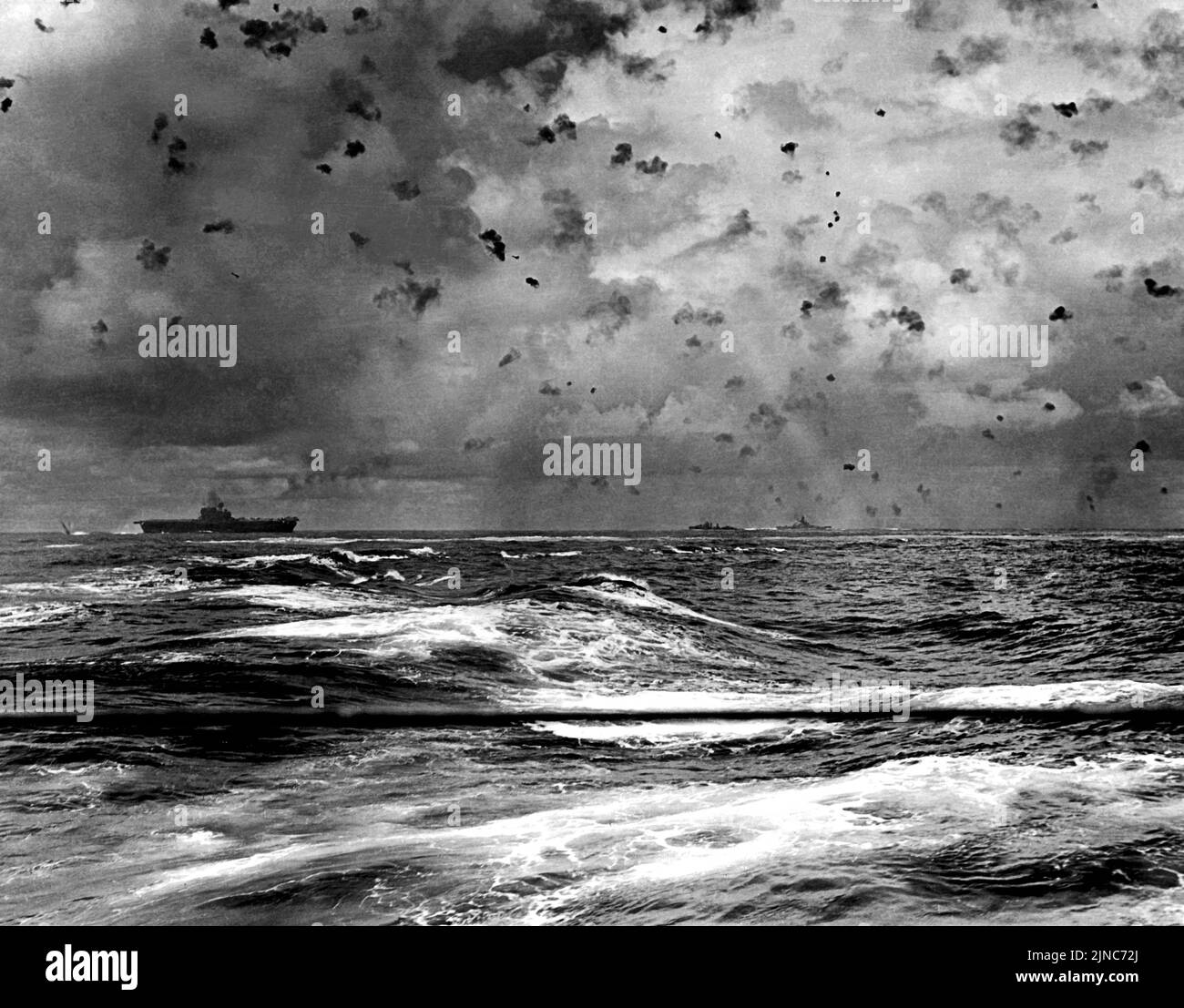 En una foto dramática de la acción el portaaviones USS Enterprise (CV-6) de la Marina de los EE.UU. Y otras naves de su pantalla en acción durante la Batalla de Santa Cruz, el 26 de octubre de 1942. Una bomba está explotando desde su popa, mientras que dos bombarderos de buceo japoneses son visibles directamente sobre el portador y hacia el centro de la imagen. Foto de stock