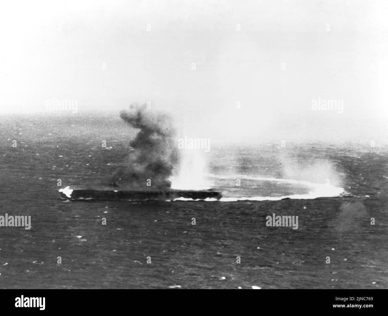 El portaaviones japonés Shōkaku, a gran velocidad y con un giro duro, ha sufrido ataques con bombas y está en llamas durante la Batalla del Mar de Coral en mayo de 1942. Foto de stock
