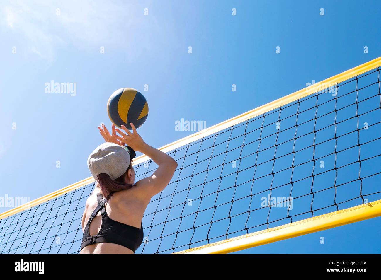 Las vacaciones de verano, el deporte y la gente concepto. joven con bola jugando voleibol en la playa. tirar la bola a través de la red de voleibol. Foto de stock