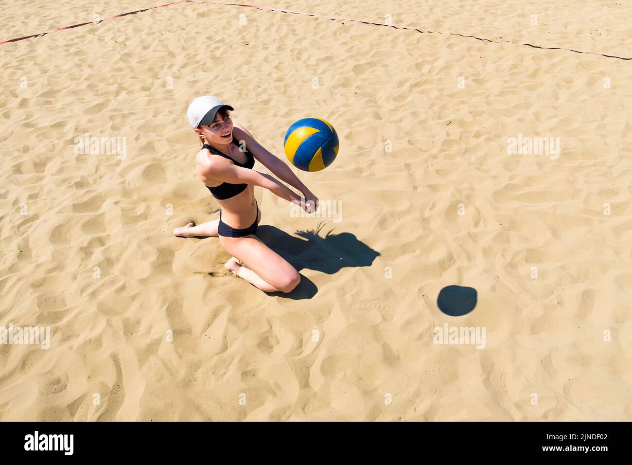 la chica coge la pelota en la arena jugando al voleibol de playa. Juegos deportivos al aire libre. Concepto de un estilo de vida saludable. Foto de stock