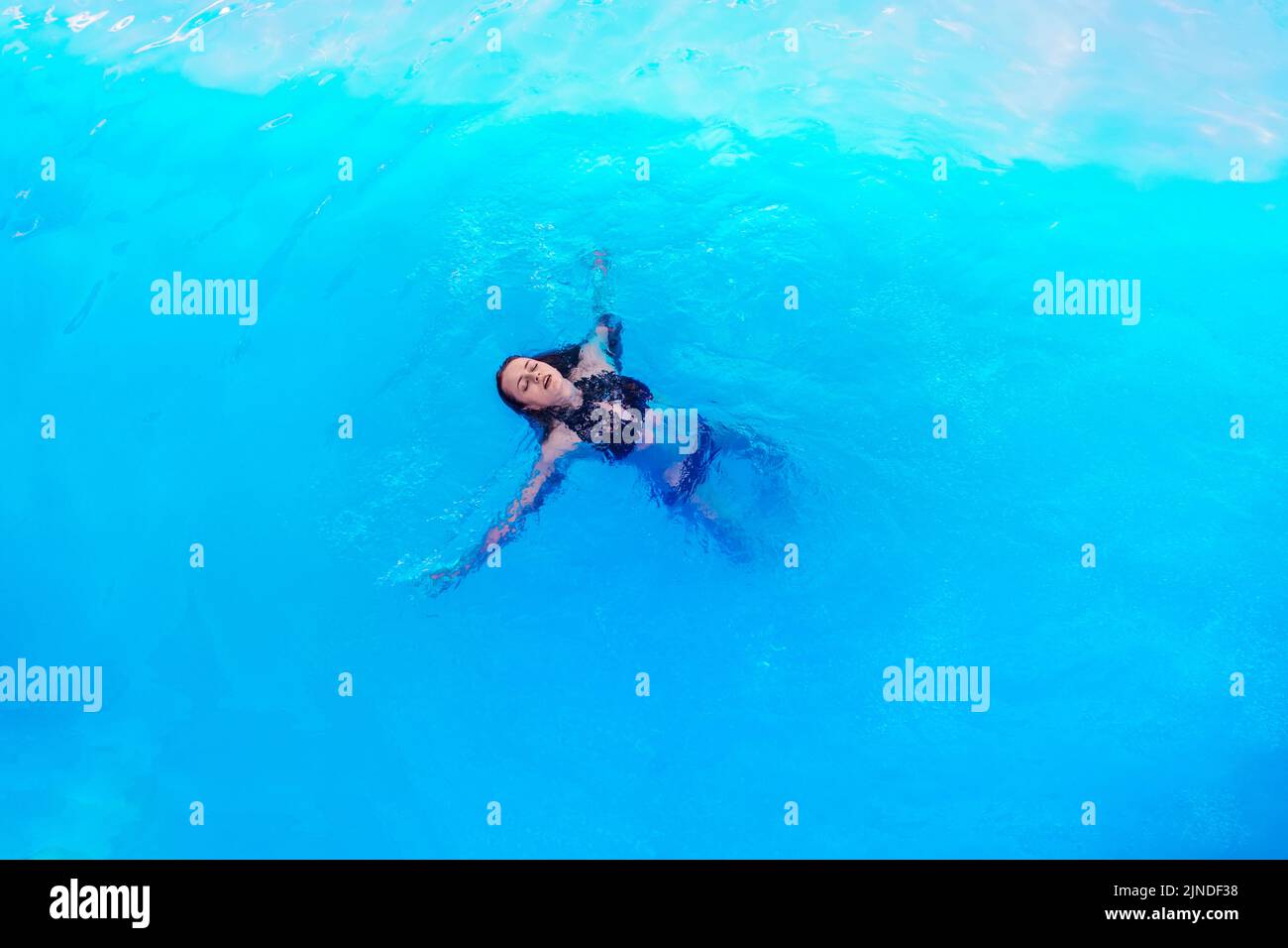 Mujer hermosa en una piscina. Chica en traje de baño negro y gafas de sol nada en su espalda en agua clara en la piscina Foto de stock