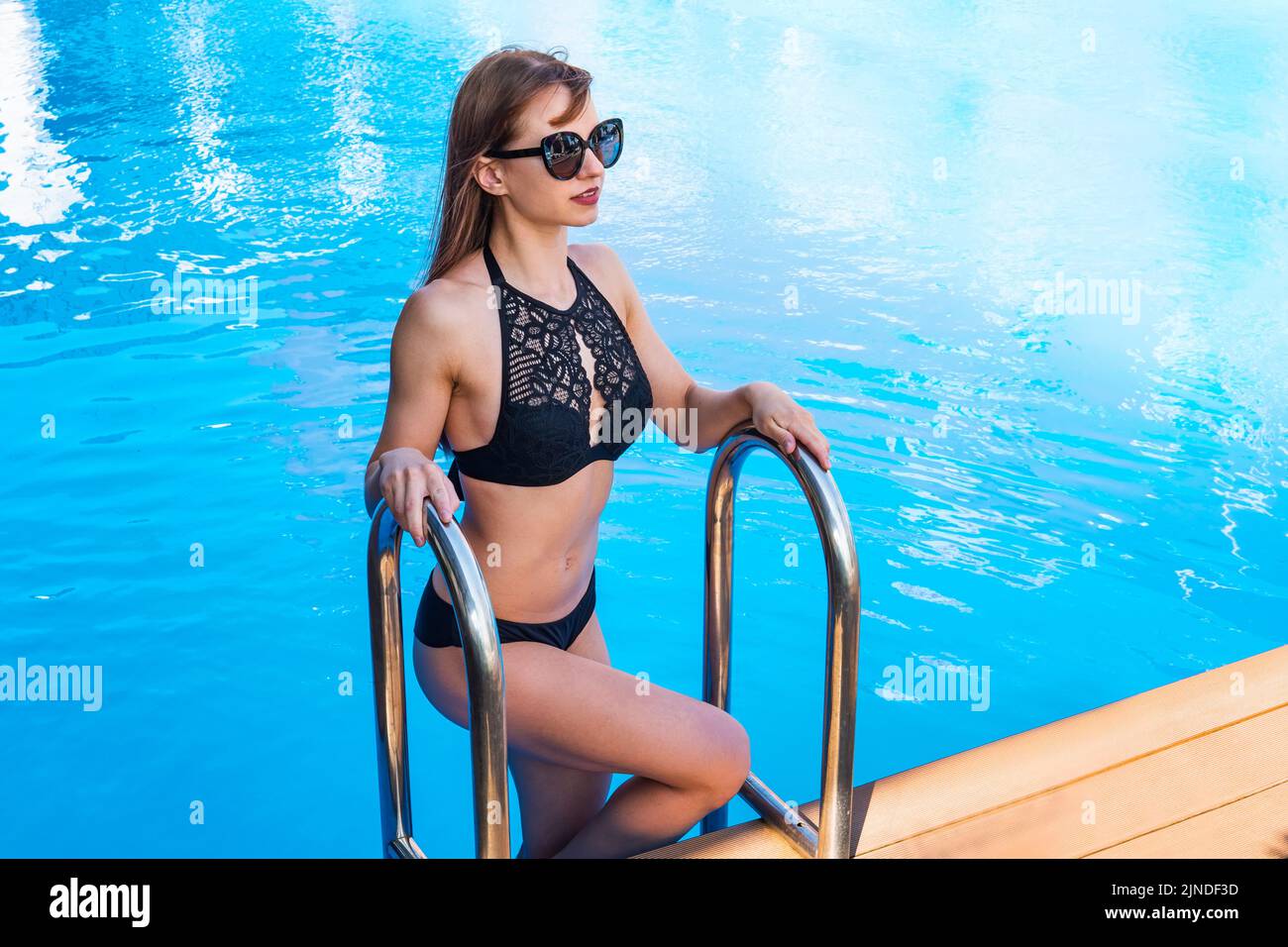 hermosa mujer saliendo de la piscina. hermosa modelo femenino de pelo largo bronceado posando junto al agua azul de la piscina. Retrato de verano al aire libre de chica sexy Foto de stock