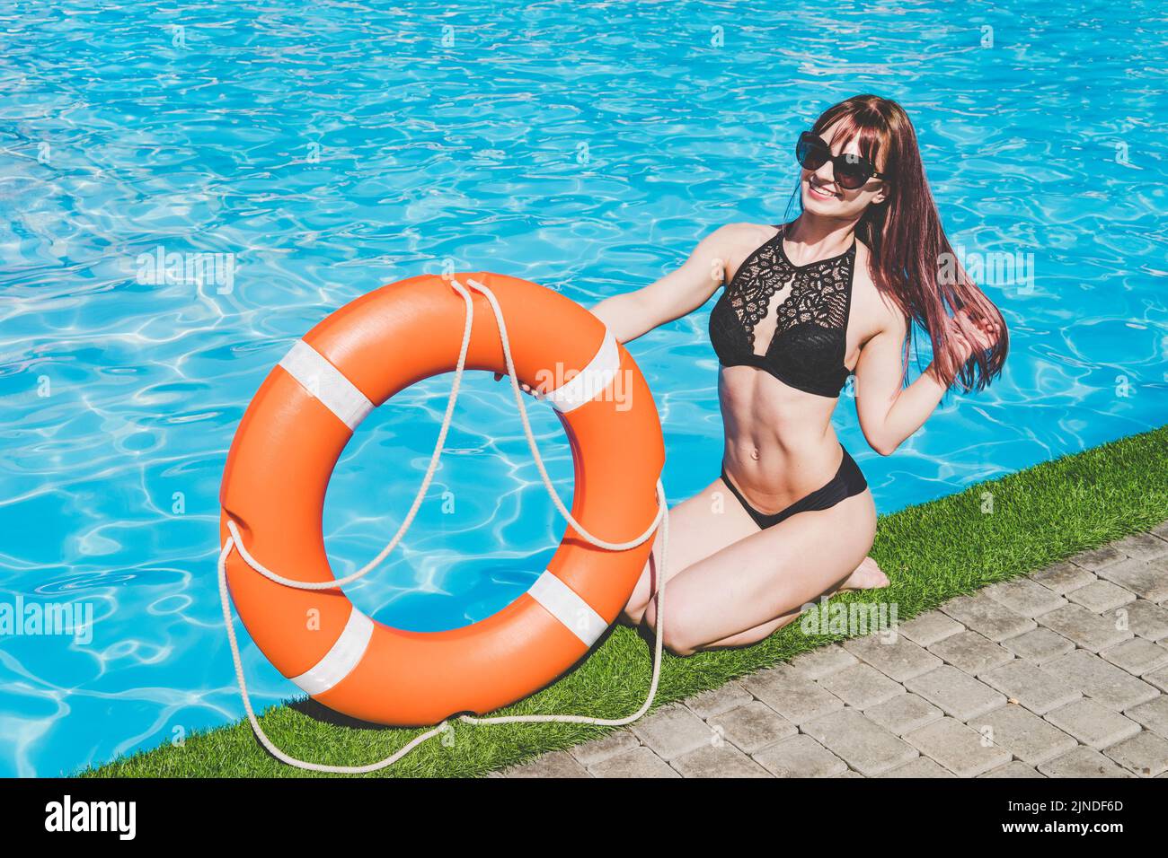 Chica con un salvavidas cerca de la piscina en el fondo de aguas azul claro Foto de stock