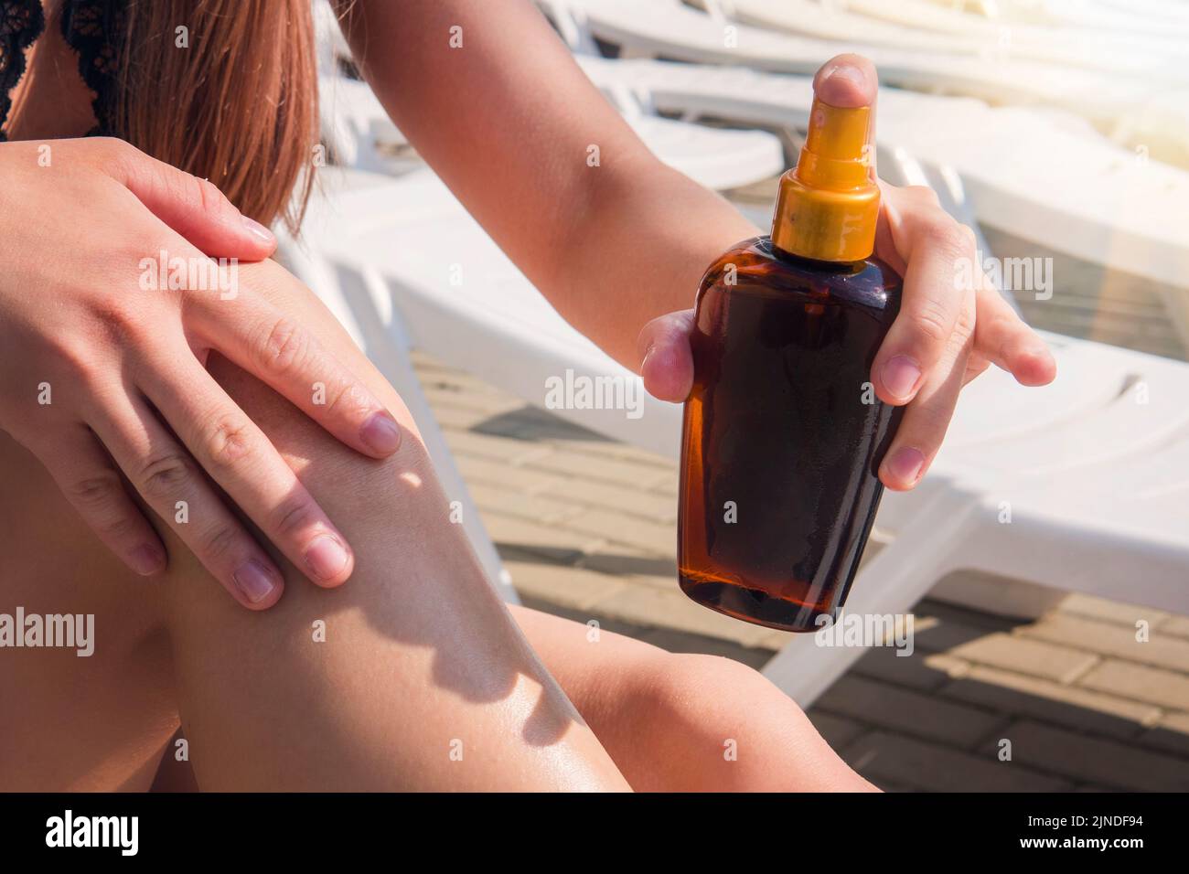 Lady está masajeando loción solar mientras toma el sol. Modelo femenino durante las vacaciones de verano. Crema solar bronceadora en botella de aerosol. Mujer joven en spra Foto de stock