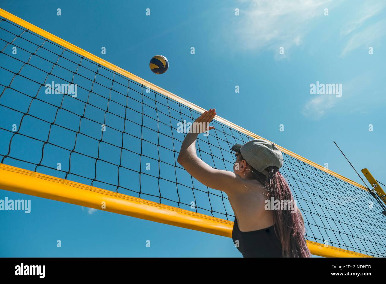 Salto de voleibol de playa jugador femenino. La mujer alcanza para la bola. Lanzando un voleibol amarillo sobre la red. Punto de victoria. Juegos de deportes al aire libre Foto de stock