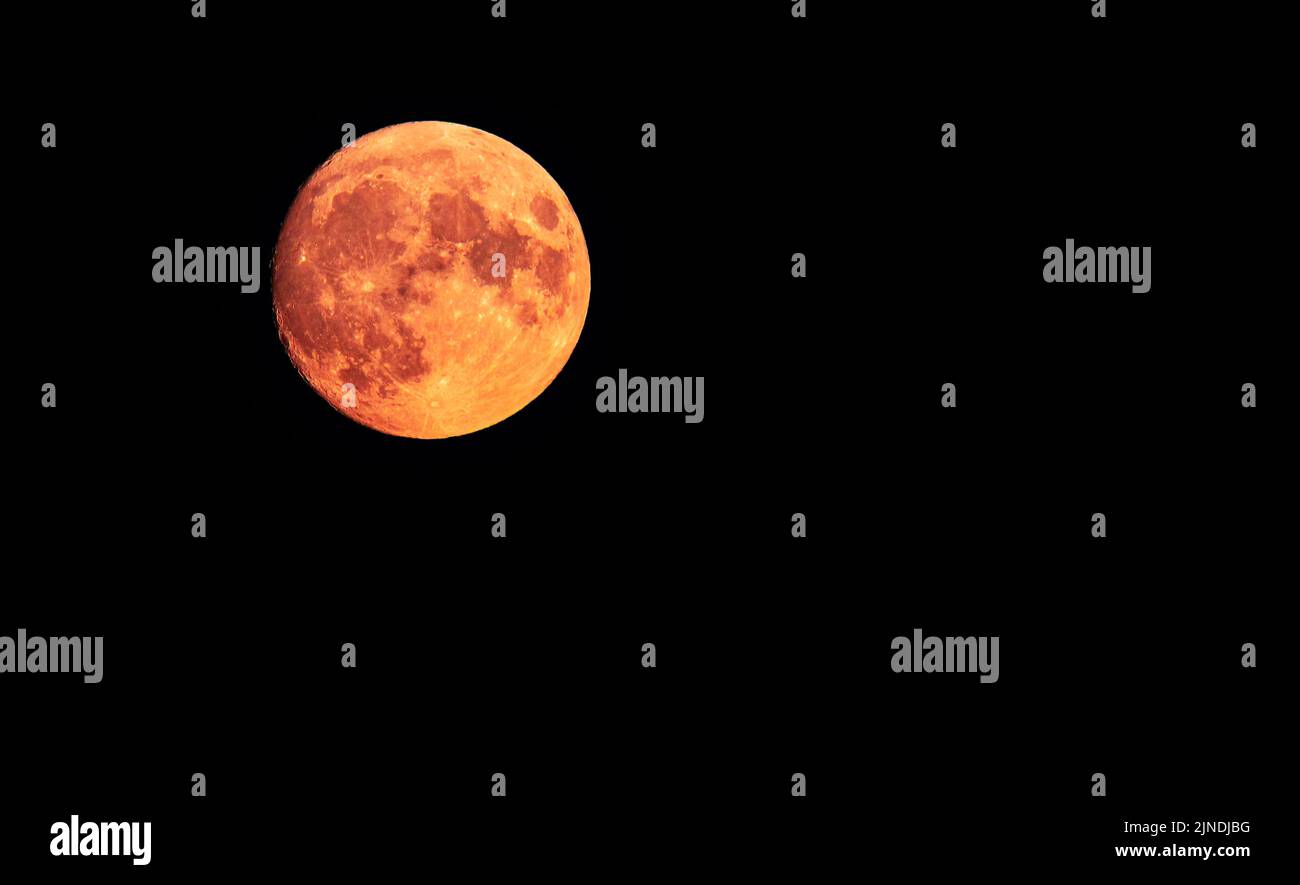 La luna Gibbous encerando en 97,5% lleno, rojo brillante y naranja, 2022 de agosto, justo sobre el horizonte de la costa sur del Reino Unido. Con copyspace (espacio COPE). Foto de stock