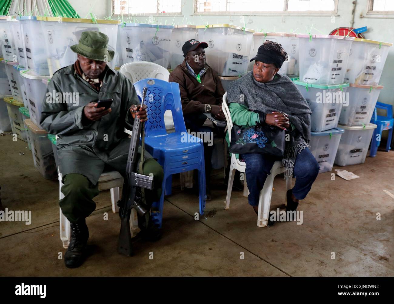 Un oficial de policía se sienta al lado de los agentes electorales cerca de urnas selladas que contienen material electoral en un centro de conteo de la Comisión Electoral Independiente y de Fronteras (IEBC) después de las elecciones generales en Nairobi, Kenia, el 11 de agosto de 2022. REUTERS/Thomas Mukoya Foto de stock