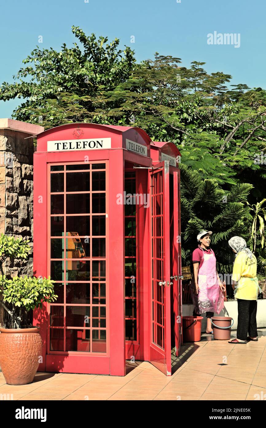 Mujeres que mantienen una conversación en el lado de una caja telefónica roja fuera de servicio en Kota Kinabalu, Sabah, Malasia. Foto de stock