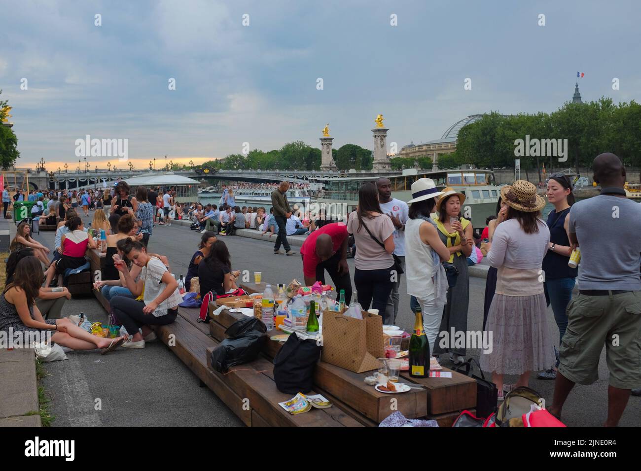 La gente, en su mayoría turistas, se socializan con la comida y el vino a lo largo de la ribera del Sena, por Pont Alexandre III Hermoso día de verano al aire libre en París, Francia. Foto de stock