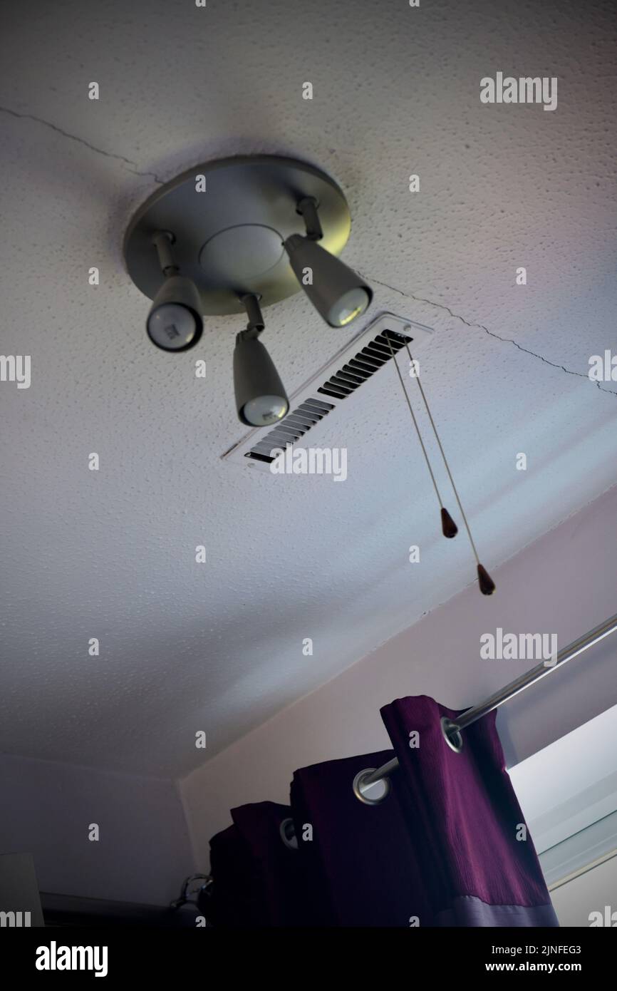 la luz central del techo agrietado y la salida de la calefacción central en el techo revestido de artex Foto de stock