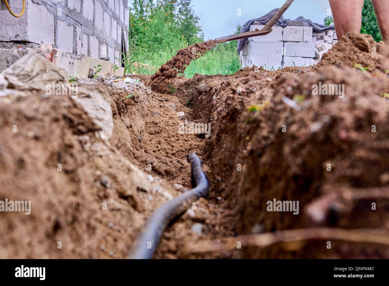 El trabajador de la construcción está cavando trincheras para colocar cables, usando una pala para excavar el suelo. Foto de stock