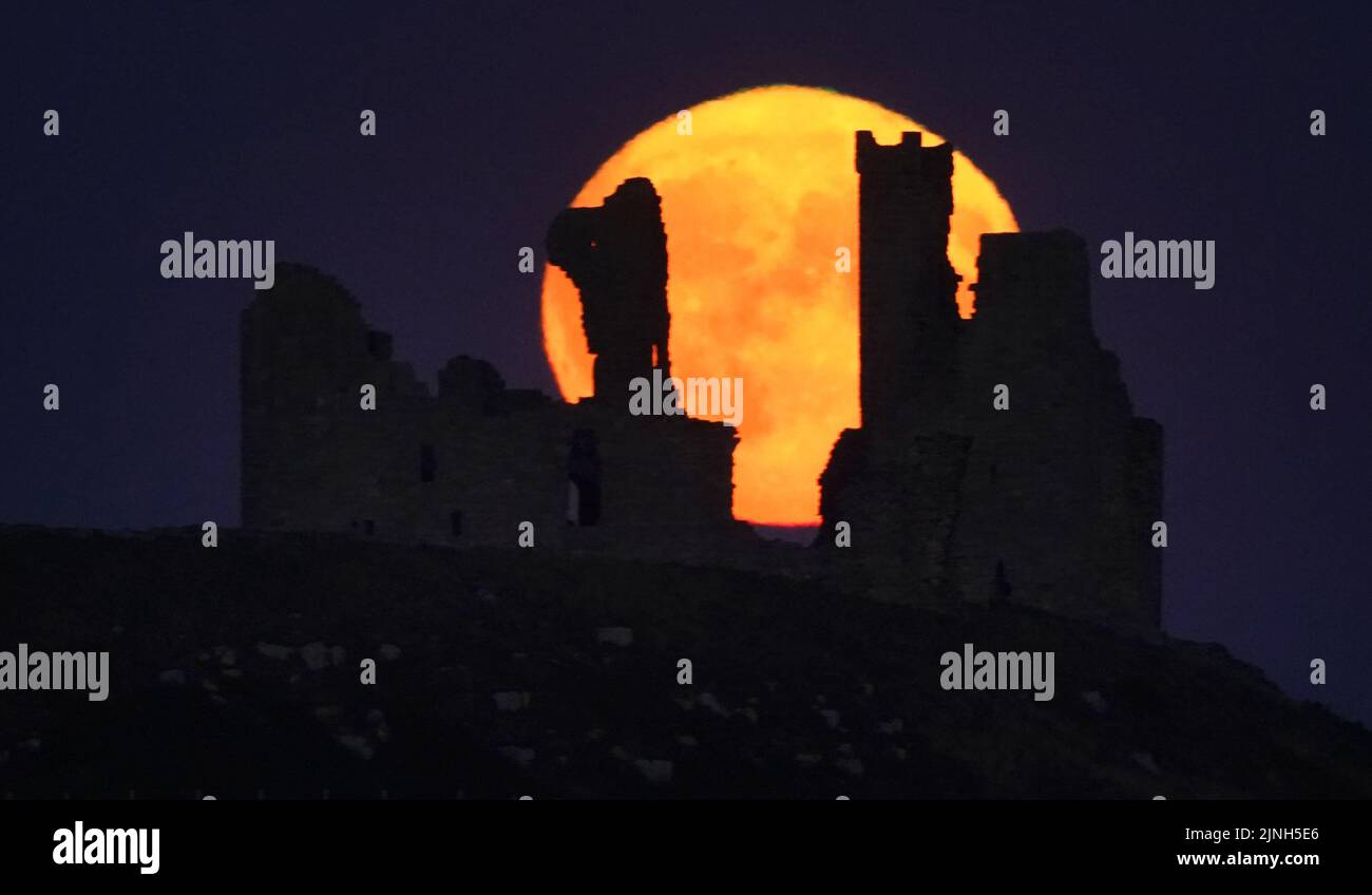 La superluna Sturgeon, la superluna final del año, se eleva sobre el Castillo de Dunstanburgh en Northumberland. Fecha de la foto: Jueves 11 de agosto de 2022. Foto de stock