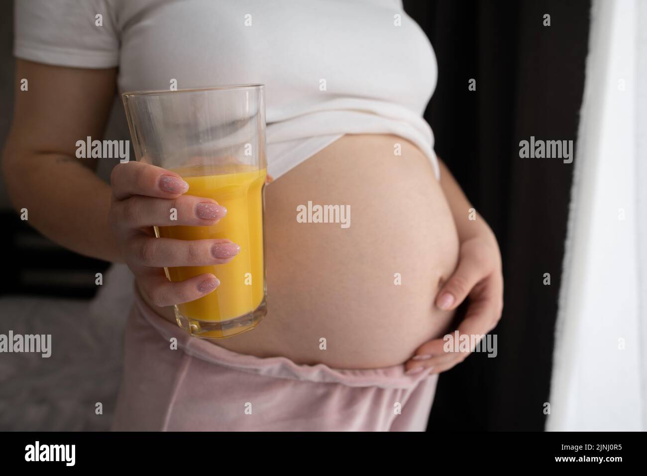Primer plano mujer embarazada con un vaso de jugo de naranja, embarazo salud y dieta oncept Foto de stock