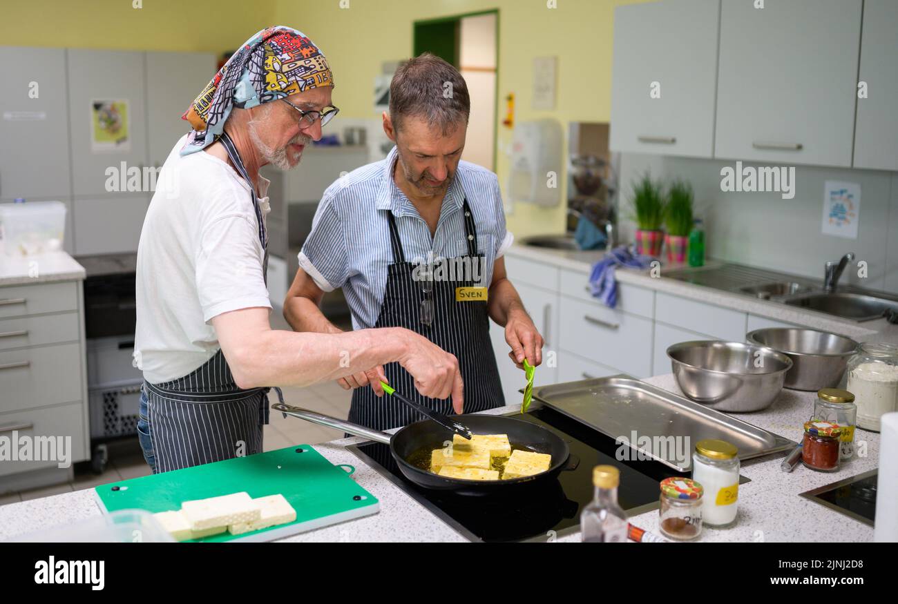 PRODUCCIÓN - 30 de junio de 2022, Baja Sajonia, Lüneburg: Winfried Marx, chef profesional (l), da a Sven consejos sobre freír en el grupo de cocina para viudos afligidos. Los miembros del pequeño grupo, que se reúne una vez al mes en Lüneburg para cocinar, tienen entre 59 y 87 años. Un profesional guía a los viudos. (A dpa-KORR 'Grupo de cocina para viudos afligidos - las comidas listas son tabú') Foto: Philipp Schulze/dpa Foto de stock